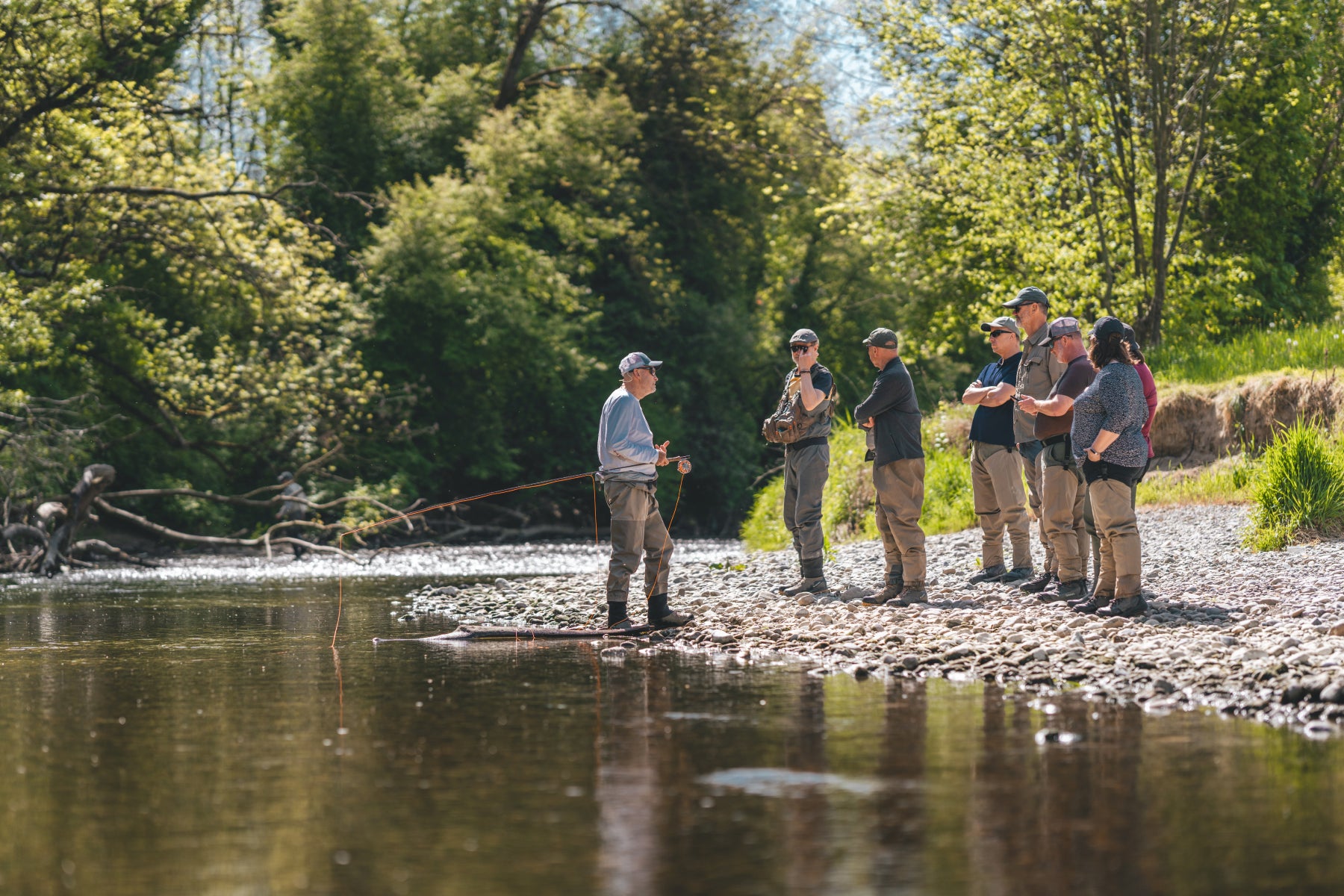 Rolf Bünter erklärt einer Gruppe von sechs Teilnehmern am Schweizer Fliessgewässer das Lesen des Wassers – Gruppen-Guiding durch Flyfishing Guide Service. Flyfishing Guide Service, Flyfish Bünti, Fliegenfischen mit Rolf Bünter, Fliegenfischen Schweiz, Gruppen-Guiding, Wasser lesen, Theorieteil am Fluss, Fliegenfischer-Gruppe, sechs Teilnehmer, Schweizer Auengewässer, Stammrevier Töss, Briefing am Wasser, Standplatz-Analyse, Fluss-Lesetechnik, Gruppentag, Fliegenfischer-Workshop
