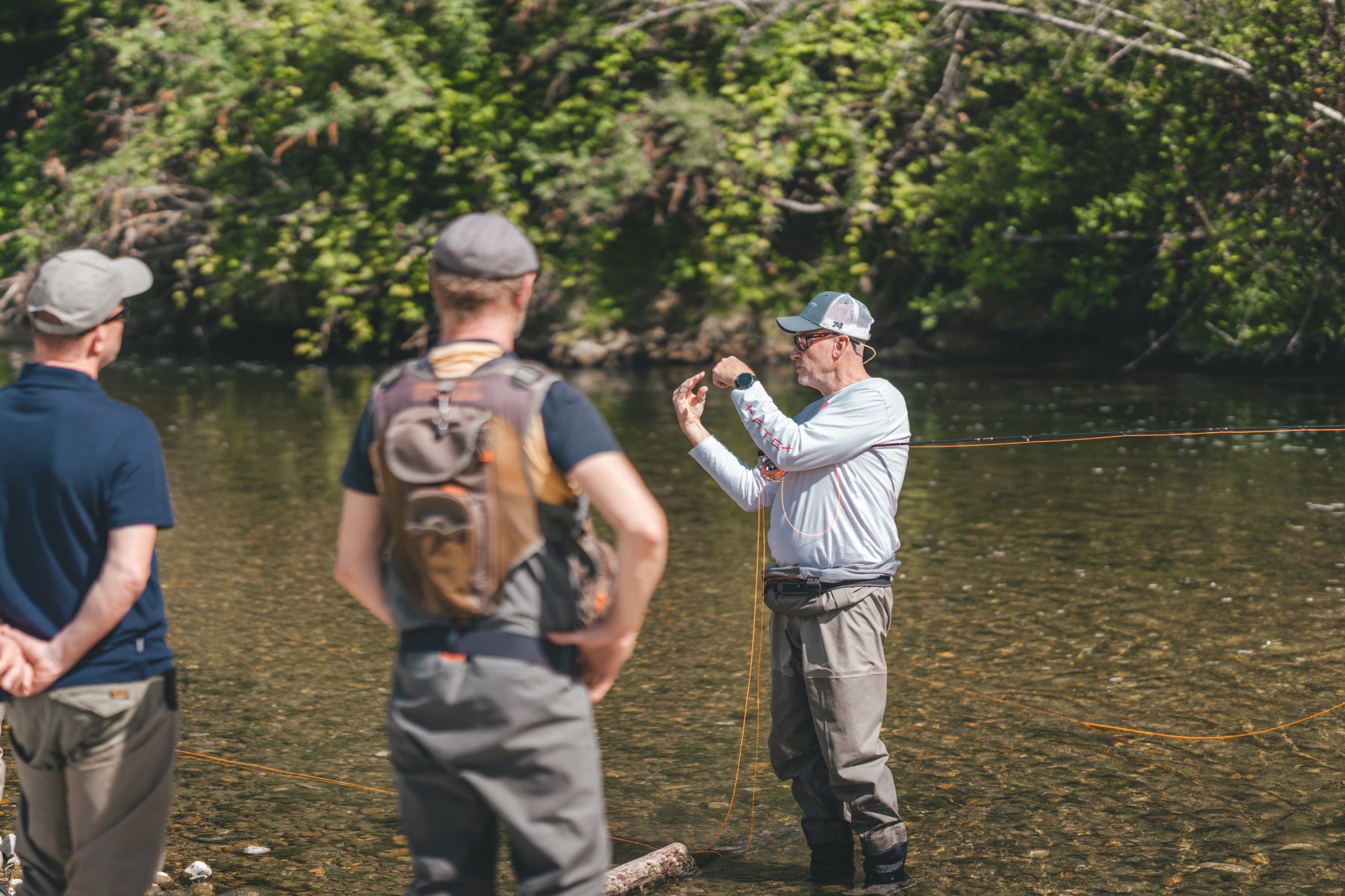 Rolf Bünter erklärt zwei Kursteilnehmern am Schweizer Fluss die Wurftechnik beim Fliegenfischen – persönliches Coaching durch Flyfishing Guide Service. Flyfishing Guide Service, Flyfish Bünti, Fliegenfischen mit Rolf Bünter, Fliegenfischen Schweiz, Wurftechnik-Coaching, Fliegenfischer-Kurs, persönliche Anleitung, Flugschnur, Watstiefel, Wurfweste, Schweizer Auengewässer, Coaching am Wasser, Anfängerkurs, Wurfschulung, Stammrevier Töss, Demonstration, Profi-Coaching, Wurftraining
