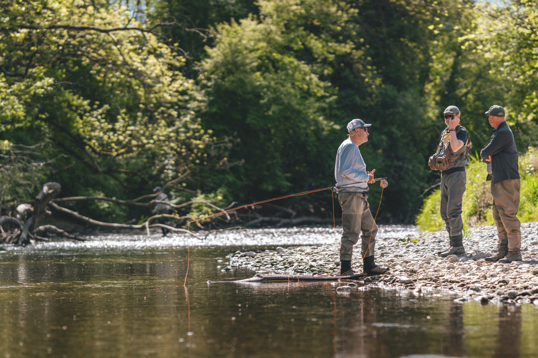 Rolf Bünter coacht einen fortgeschrittenen Fliegenfischer beim Drill mit Beobachtern am Ufer – Fortgeschrittenenkurs von Flyfishing Guide Service. Flyfishing Guide Service, Flyfish Bünti, Fliegenfischen mit Rolf Bünter, Fliegenfischen Schweiz, Drill-Coaching, Fortgeschrittene Anleitung, Beobachter am Ufer, Fliegenfischer-Profi, Watstiefel, Wurfweste, Stammrevier Töss, Drill-Technik, fortgeschrittene Praxis, Schweizer Auengewässer, Fang-Coaching, Drill am Fluss, Fortgeschrittenen-Workshop
