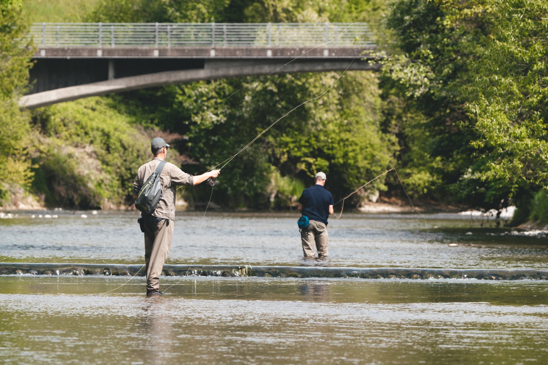 Zwei Fliegenfischer in idyllischer Flusssituation unter einer Brücke – exklusiver Privatkurs mit Flyfishing Guide Service. Flyfishing Guide Service, Flyfish Bünti, Fliegenfischen mit Rolf Bünter, Fliegenfischen Schweiz, Privatkurs Fluss, Brücke Fliegenfischen, Stammrevier Töss, exklusives Coaching, Zwei-Personen-Kurs, Sloop am Fluss, Schweizer Auengewässer, idyllische Stelle, Fliegenfischer-Atmosphäre, Privatlektion, Stille am Fluss, Brücken-Pool, Tandem-Fischen