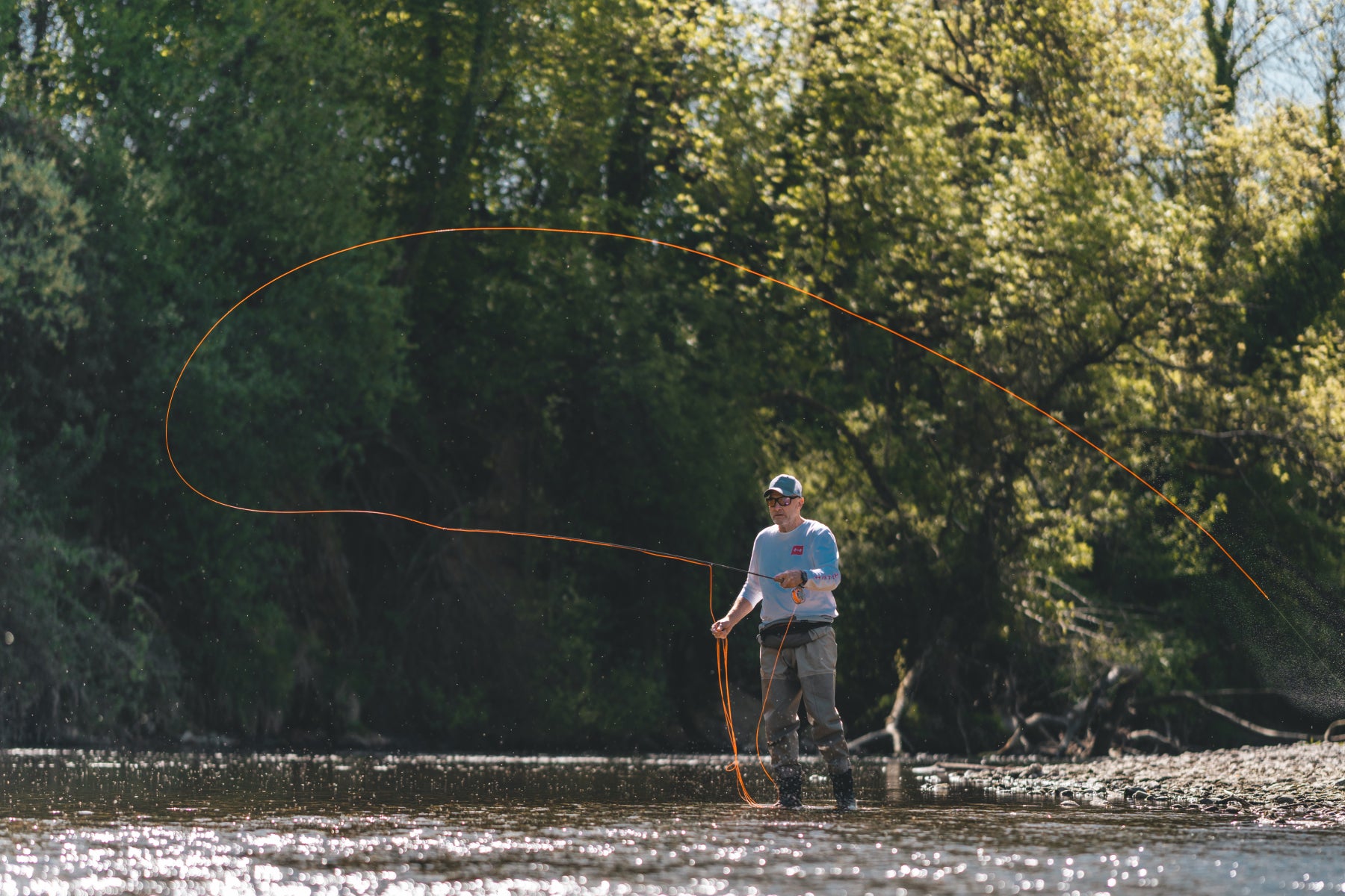 Rolf Bünter werft die Fliegenrute mit eleganter oranger Schnurschlaufe in einem Schweizer Fliessgewässer – Gründer und Inhaber von Flyfishing Guide Service. Flyfishing Guide Service, Flyfish Bünti, Fliegenfischen mit Rolf Bünter, Fliegenfischen Schweiz, Rolf Bünter Gründer, Fliegenrute Wurfschlaufe, orange Flugschnur, Schweizer Fliessgewässer, Profi-Fliegenfischer, Wurfdemonstration, Inhaber Flyfish Bünti, eleganter Wurf, Schweizer Patent, Stammrevier Töss, Wurfschule, Wurftechnik, Wurffreak, Fliegenfischer